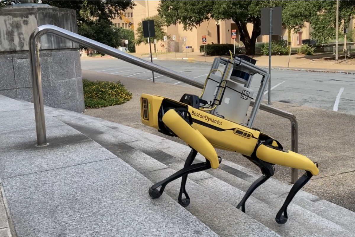 A dog-like robot ascends an outdoor staircase on a college campus.