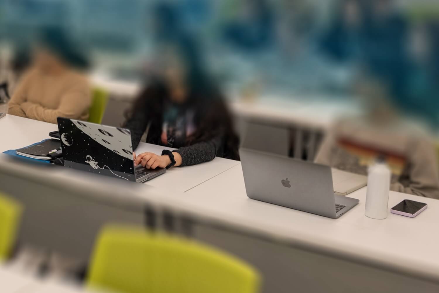 Students at laptops in a classroom sit in rows.