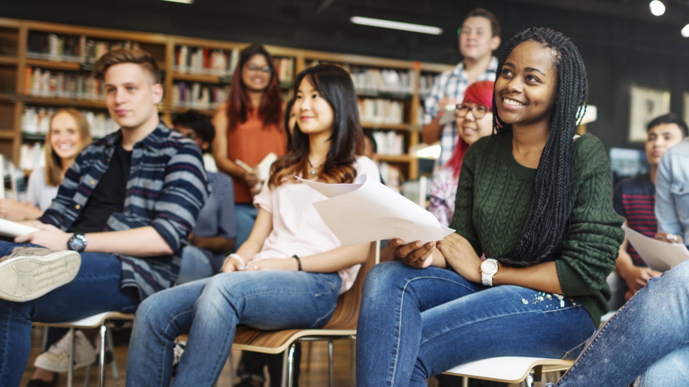 Graduate students sit and stand in rows in a library setting