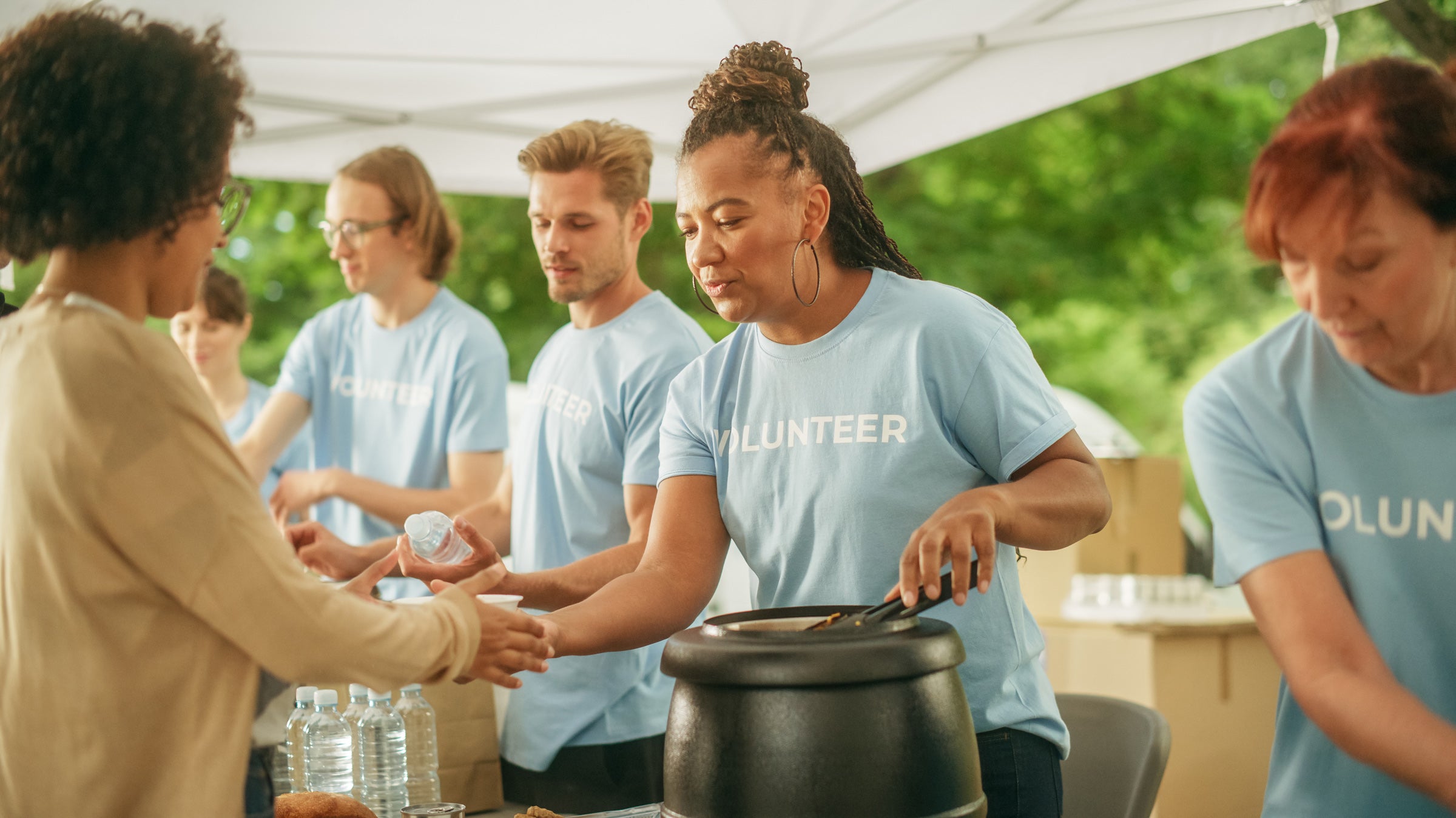 A woman wearing a blue shirt with the word Volunteer serves soup to another woman standing in line