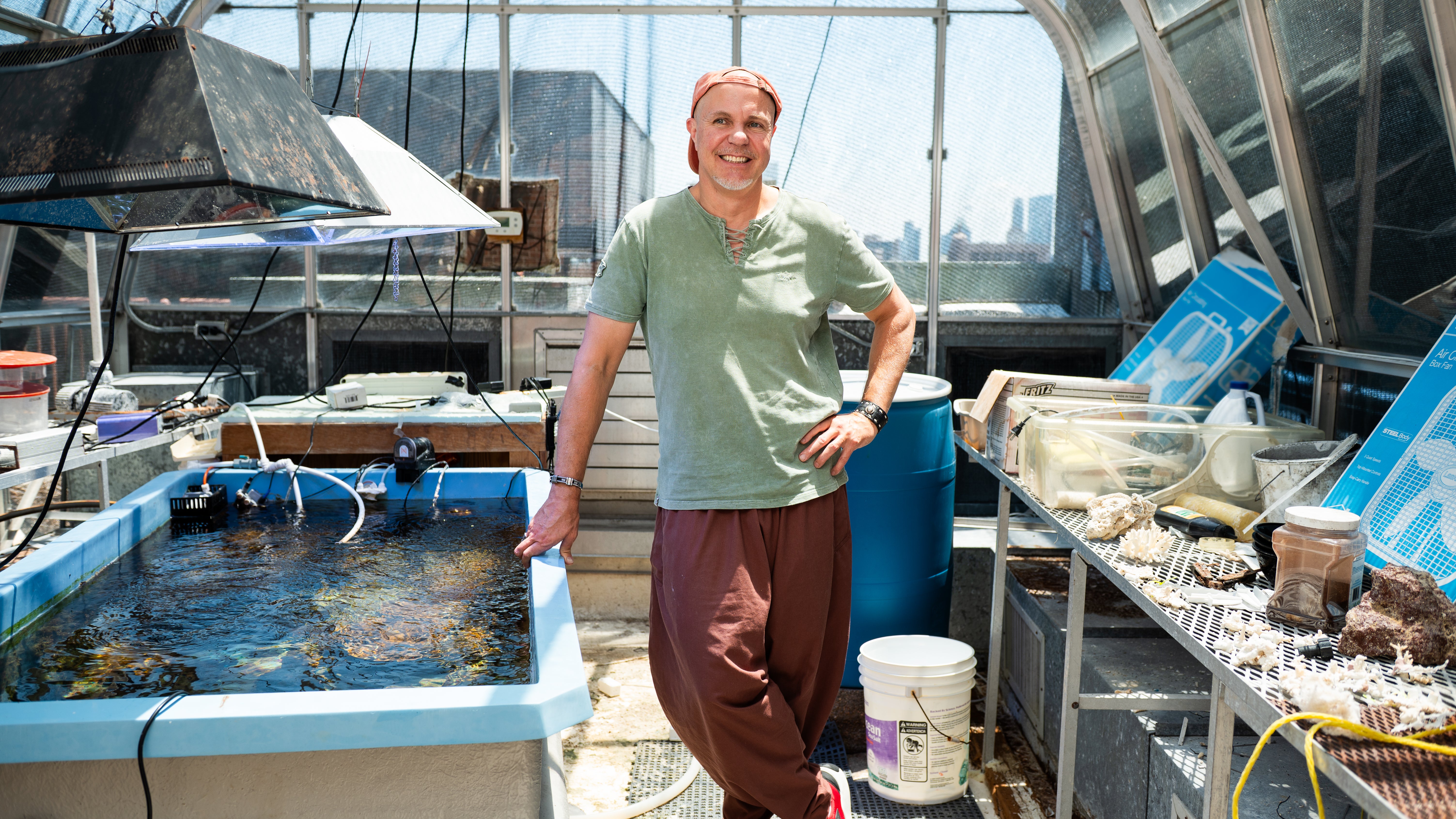A man stands in a large greenhouse next to a large tank of water containing coral