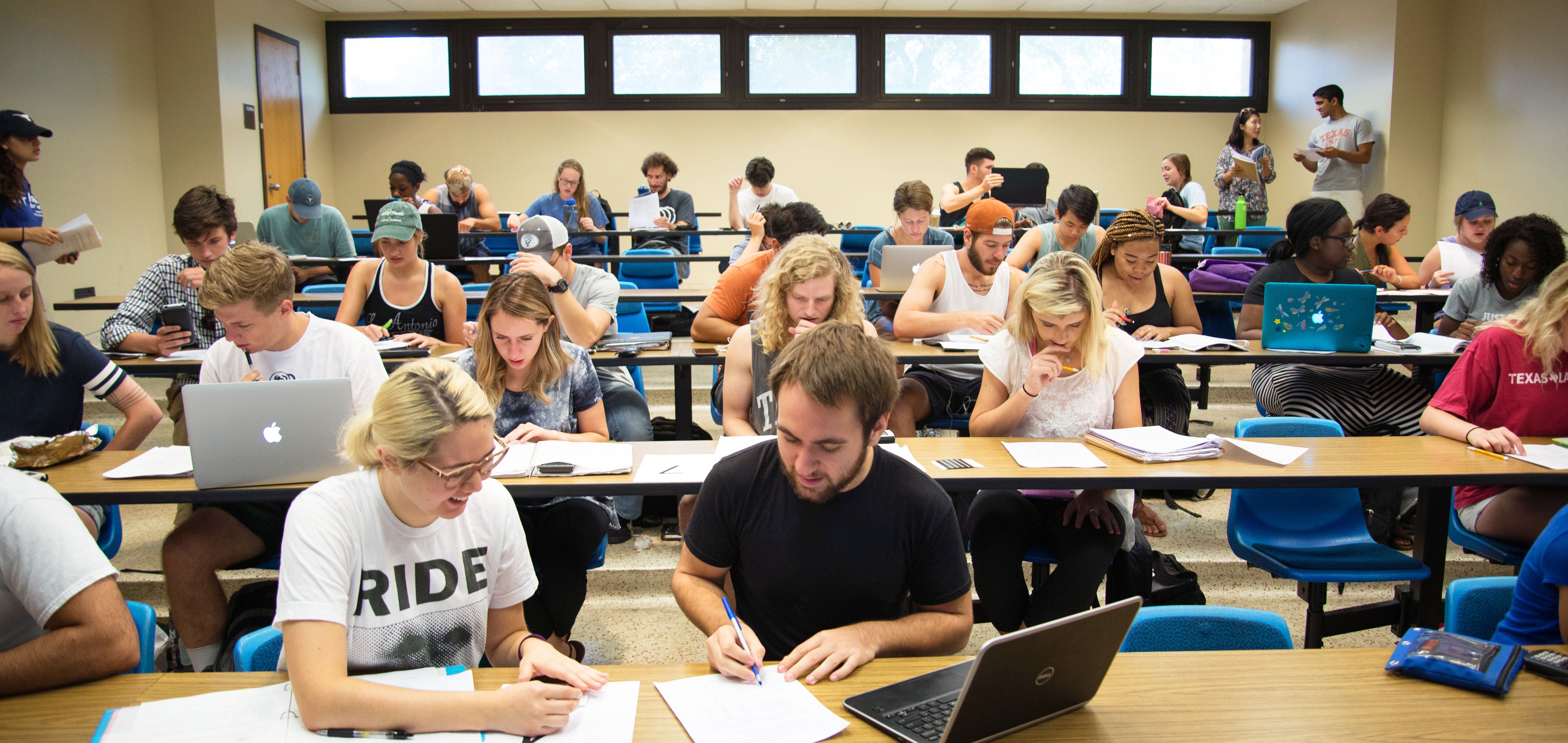 Students studying in classroom with laptops and paper on desks