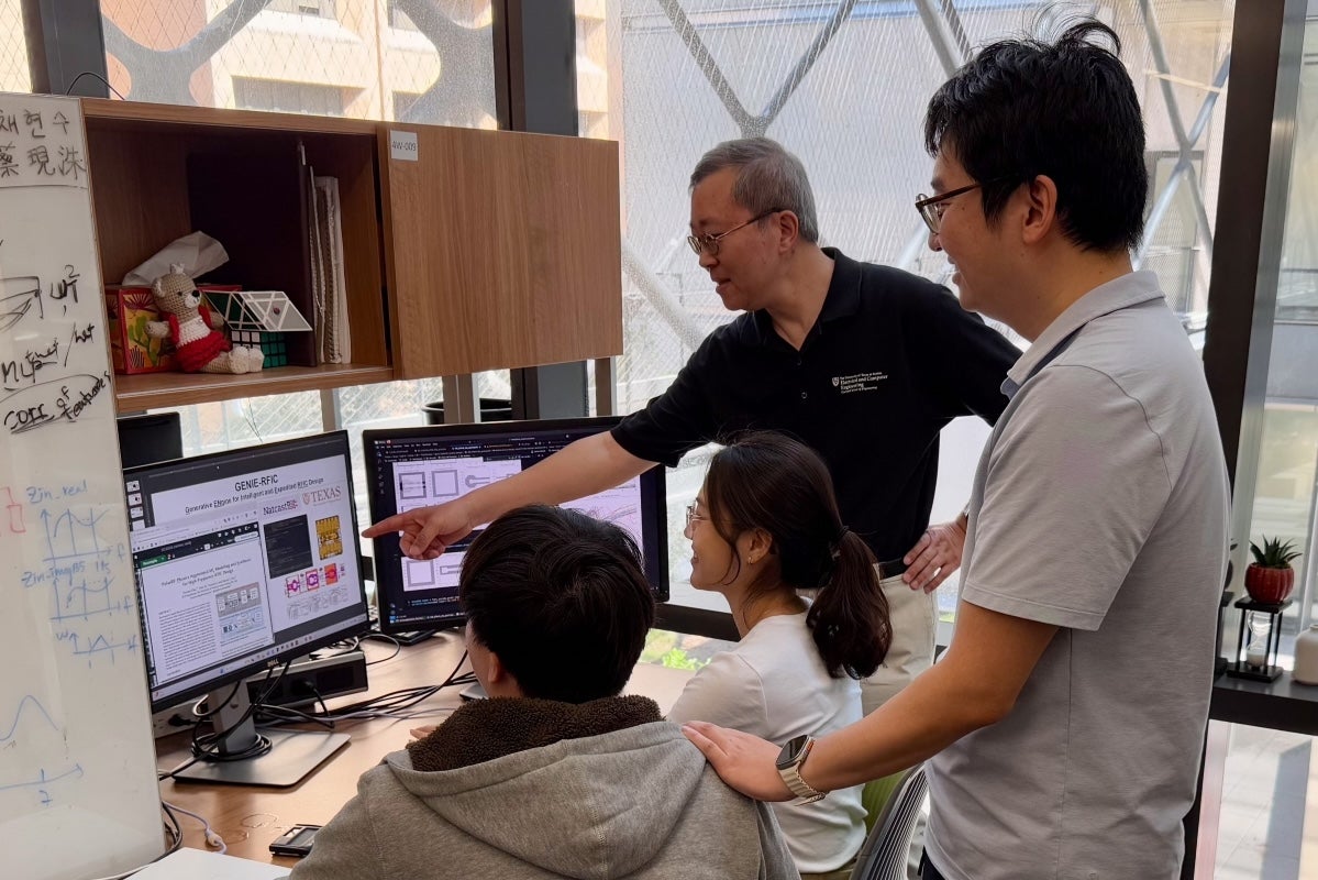 A professor in a UT electrical and computer engineering shirt points at a screen with scientific imagery, as two seated students and another researcher smile and look on.