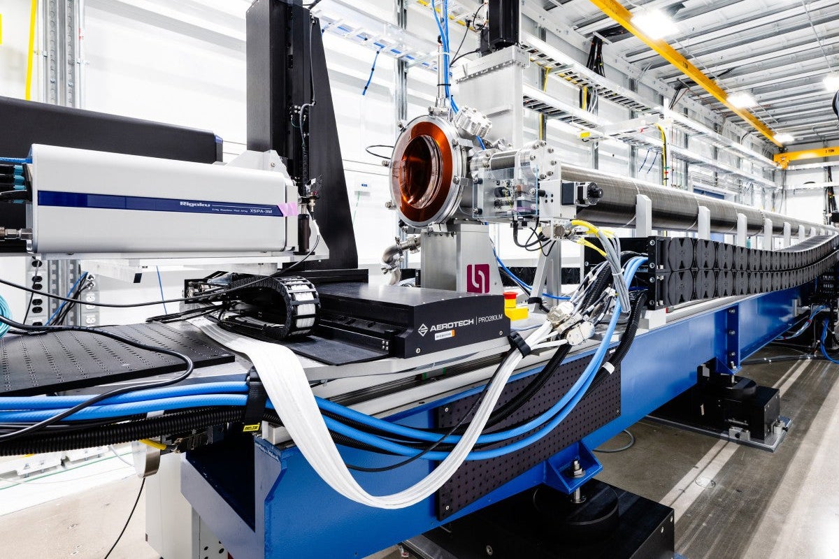 A large piece of scientific equipment with wires and metal tubes sits on a long table in a laboratory