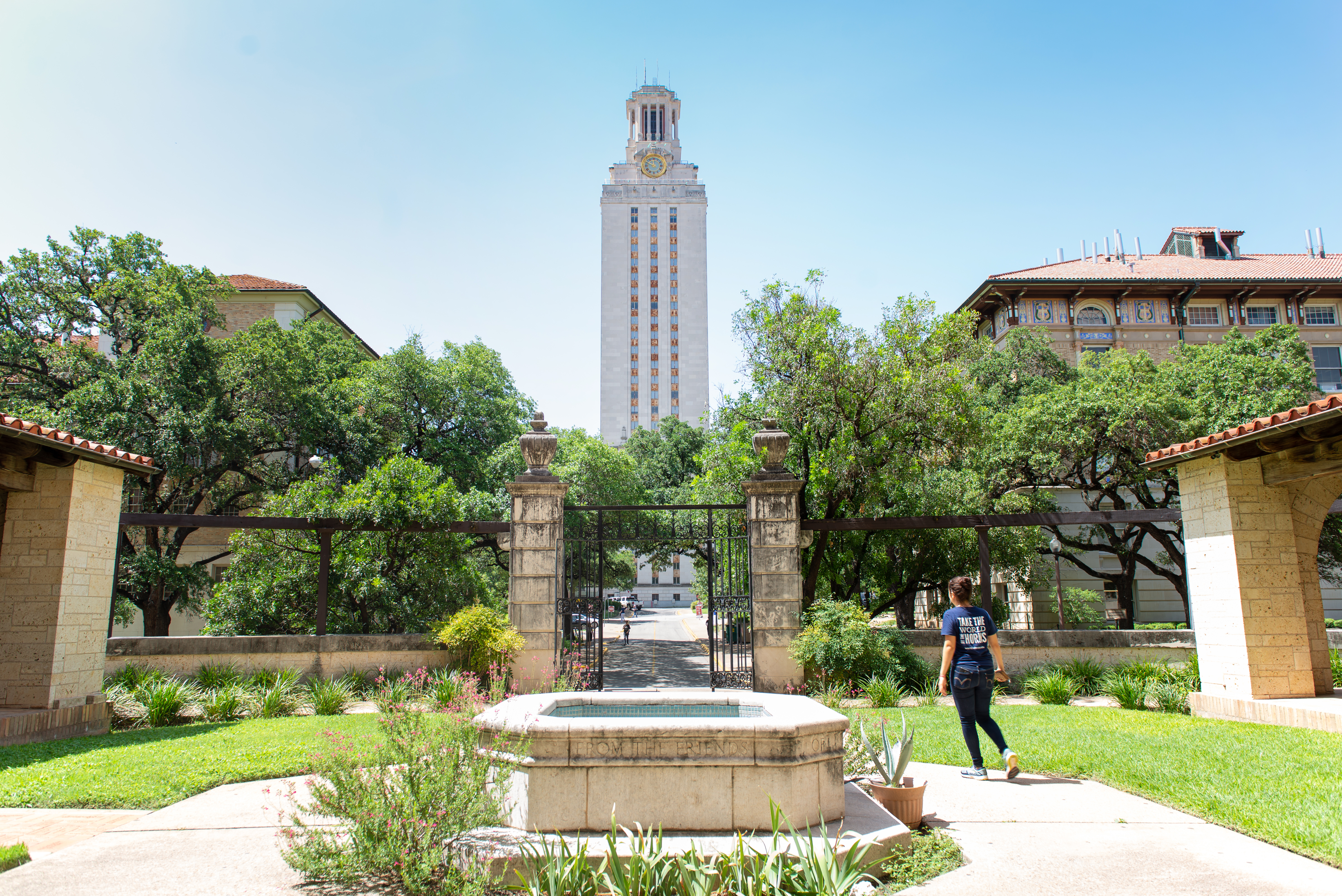 Photo of UT Tower from north with the gates of Gearing Hall and a studetn walking in the foreground.