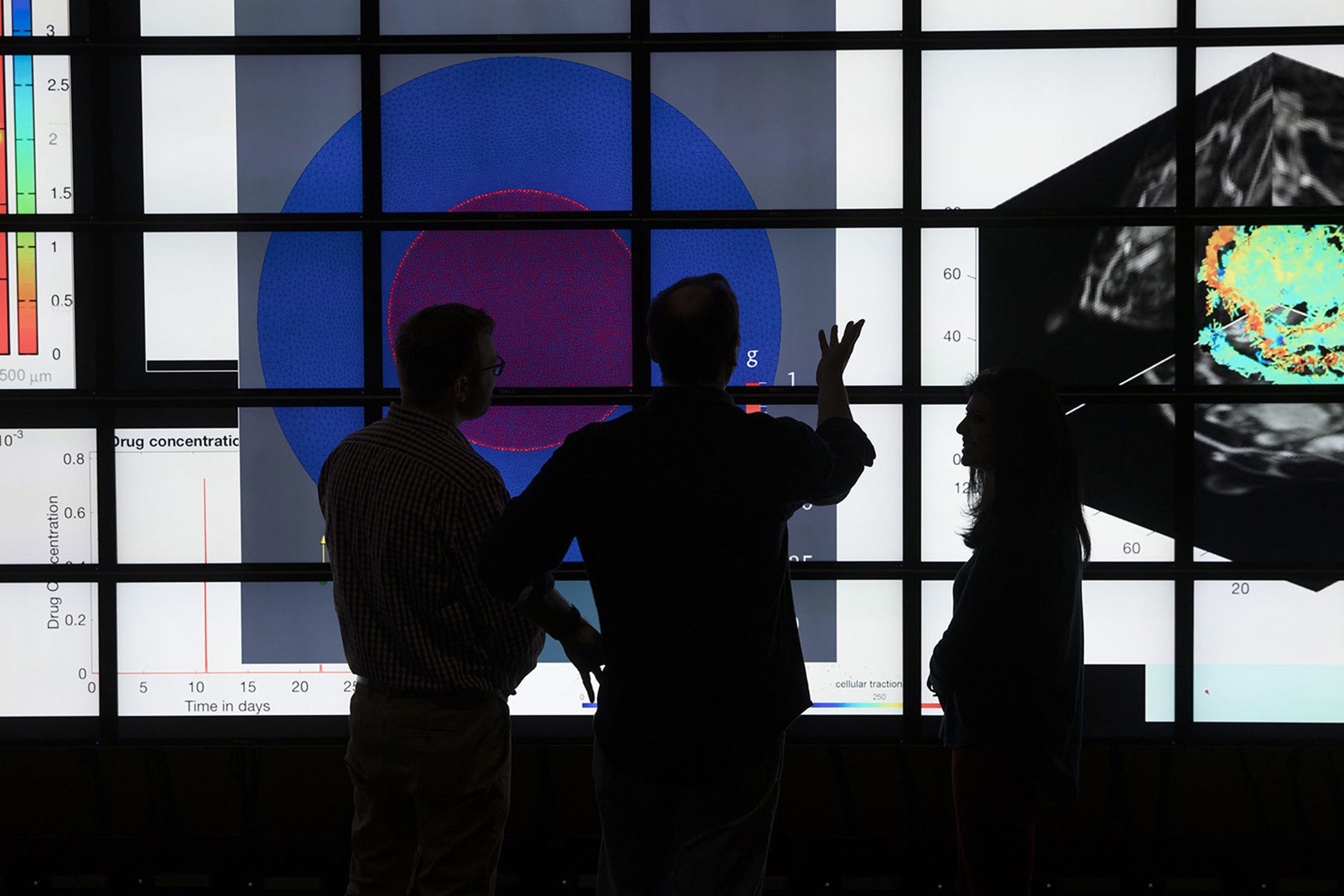 Scientists discussing data visualizations displaying on a large-scale digital screen.