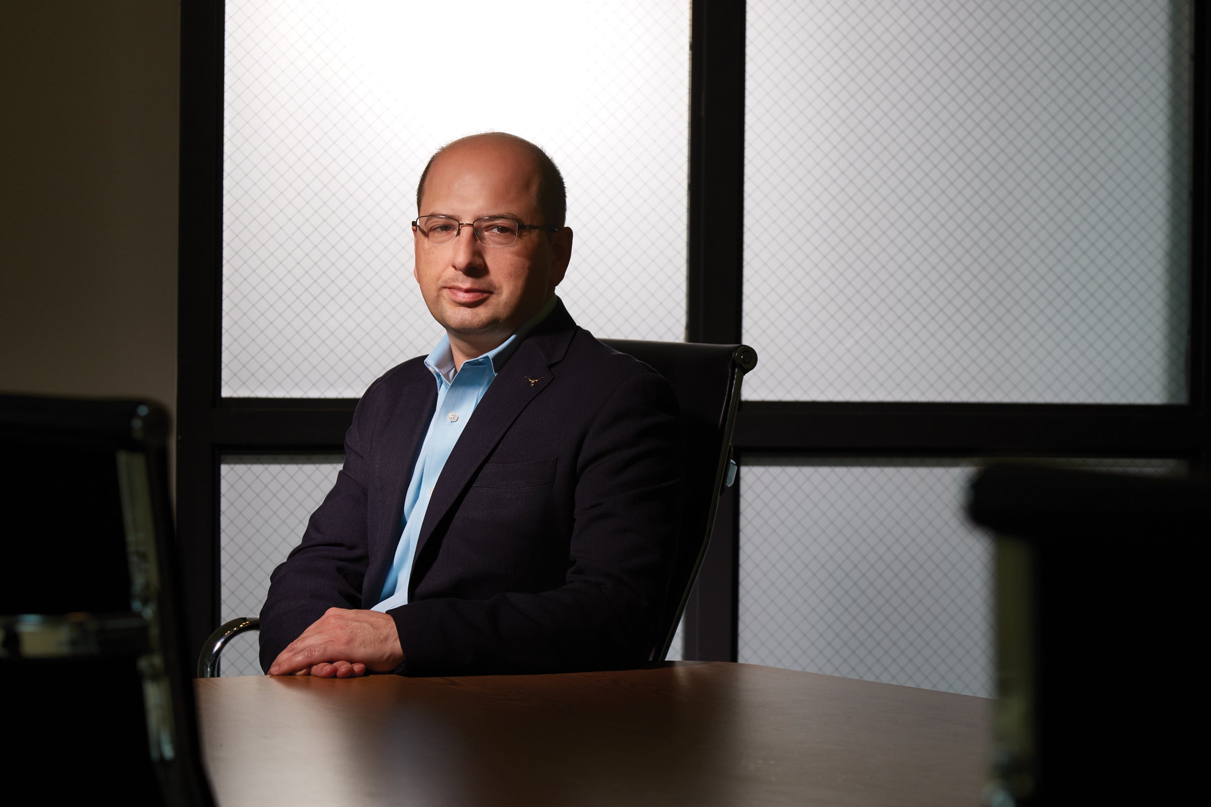 A man in a suit jacket and glasses sits at a conference table.