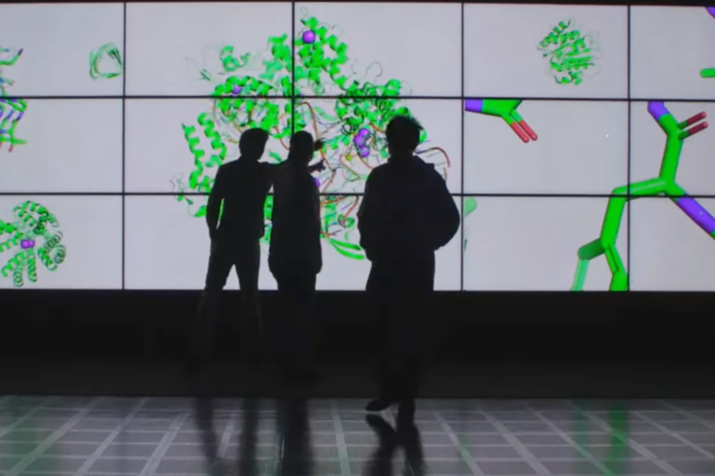 A photo of scientists observing protein structures shown on a digital display.
