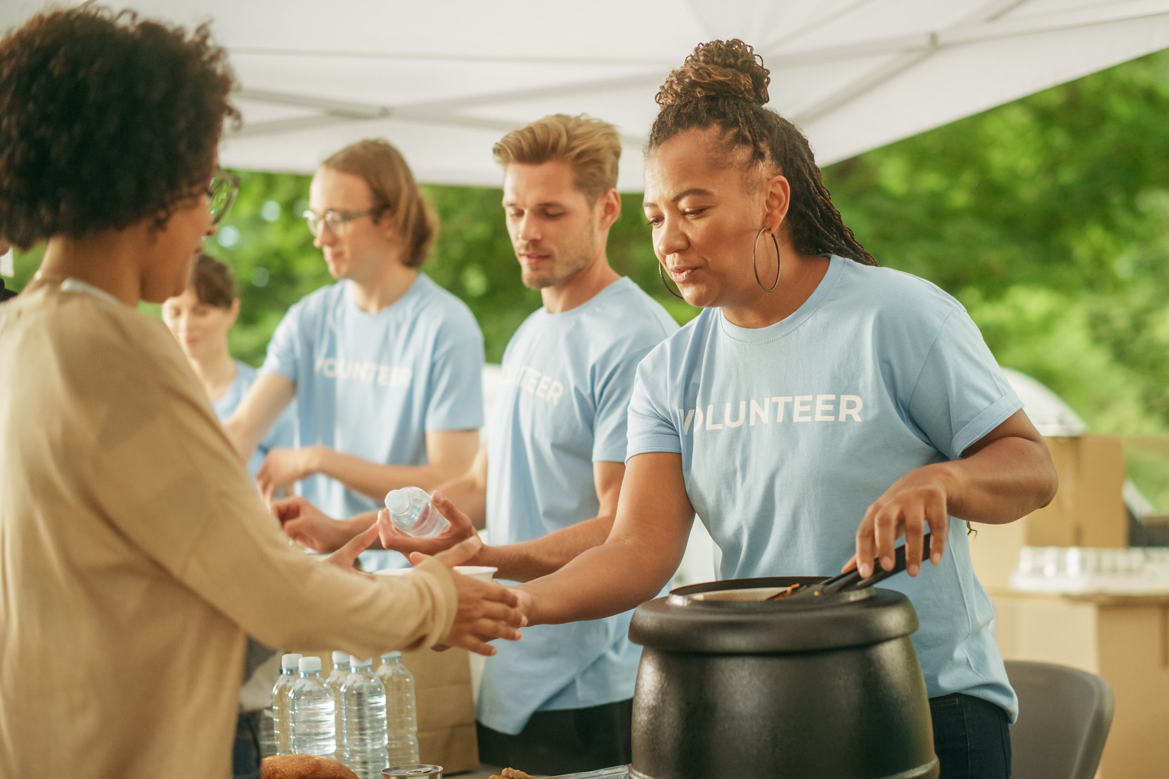 A woman wearing a blue shirt with the word Volunteer serves soup to another woman standing in line