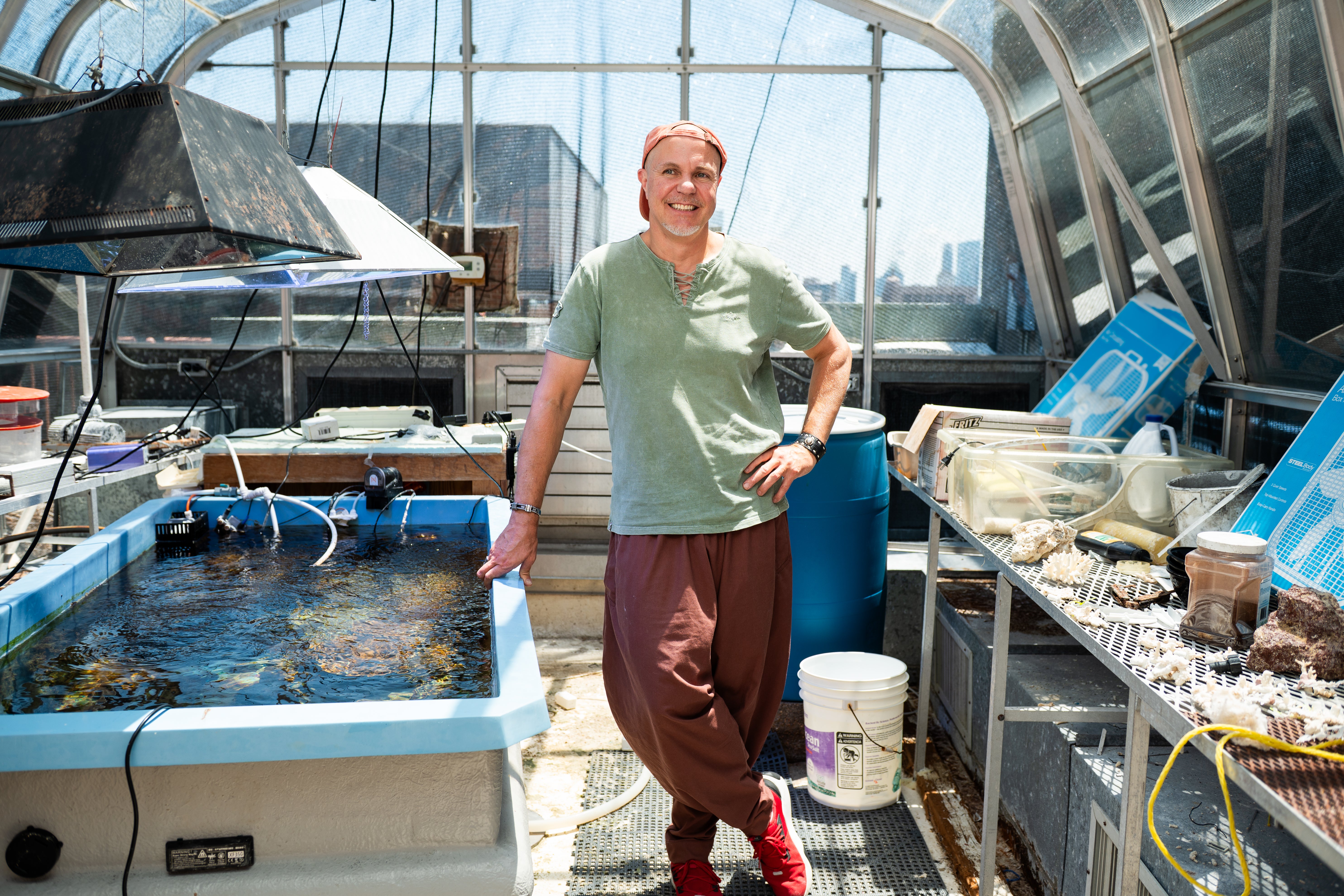 A man stands in a large greenhouse next to a large tank of water containing coral