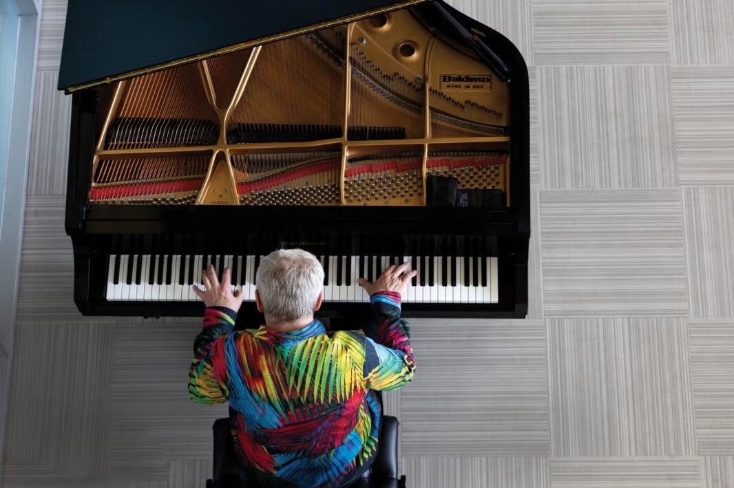 An overhead view of a man in a colorful shirt playing a grand piano