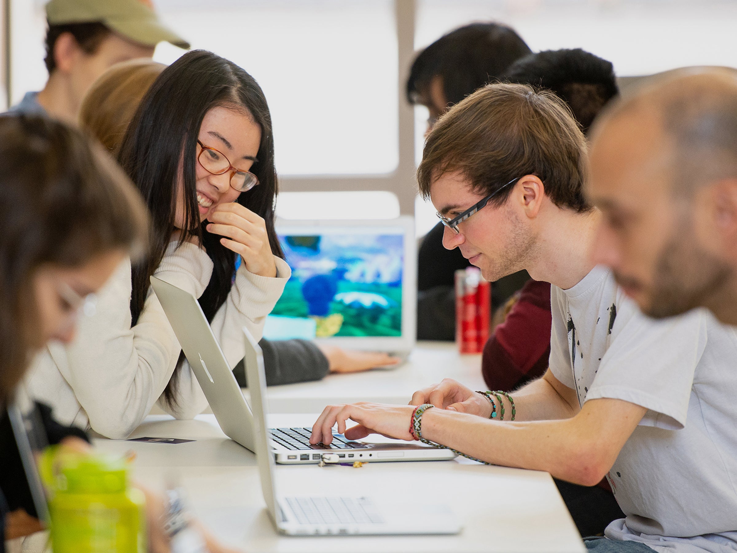 Students at a table in the GDC atrium looking at laptop computers and sharing their coding projects.