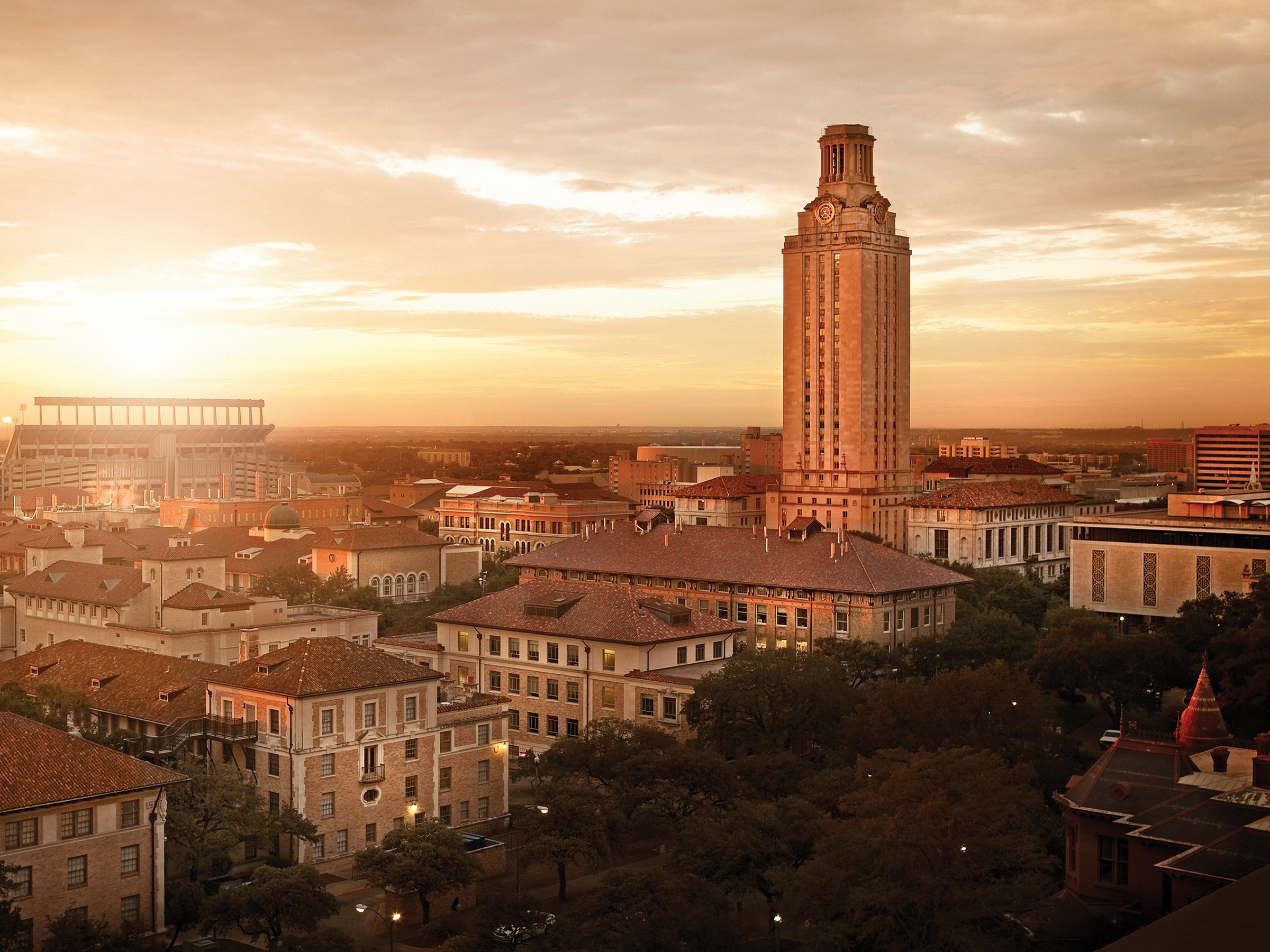 Aerial photo of UT Austin campus during sunrise with the UT Tower on the horizon in burnt orange hues.