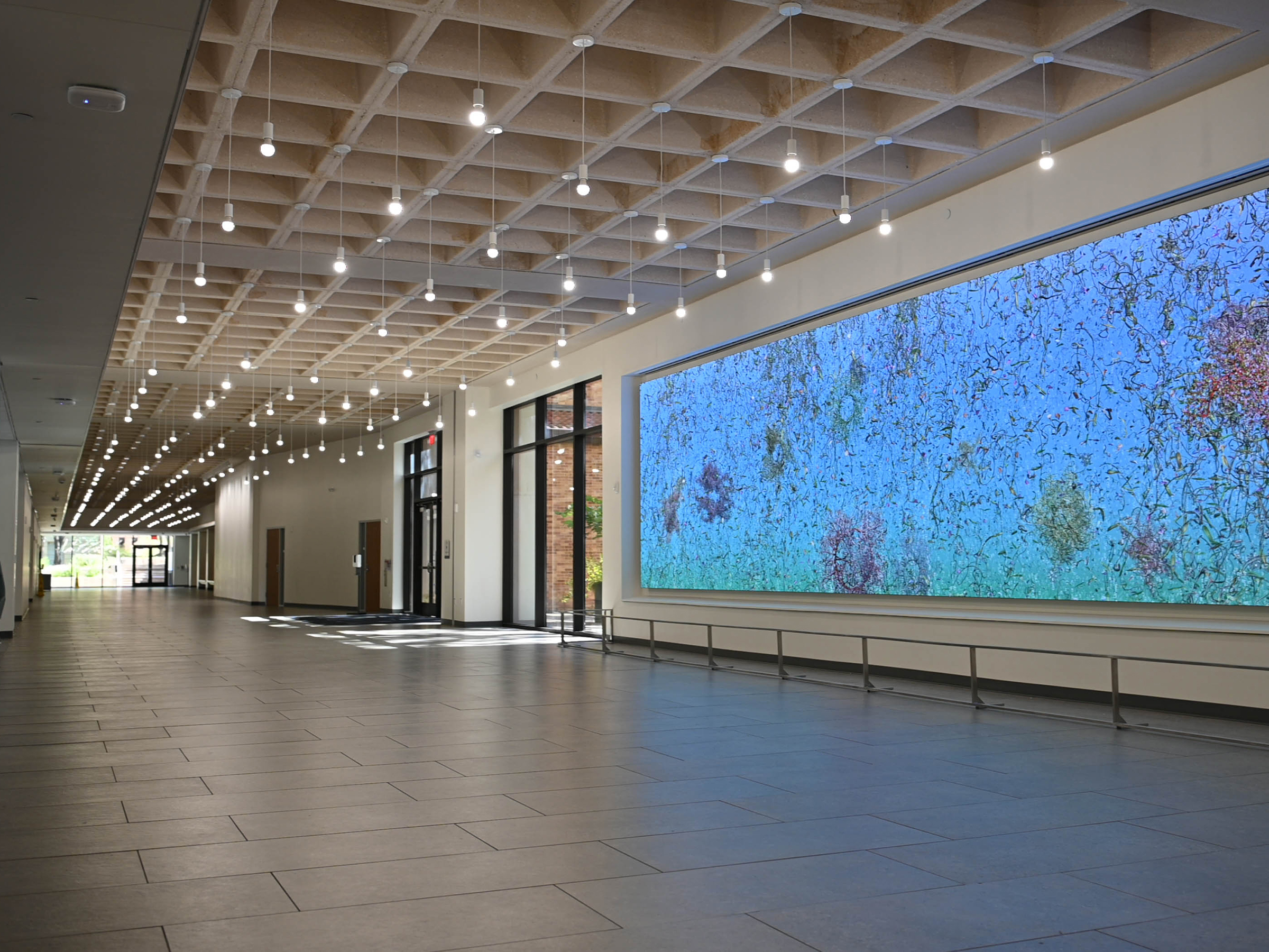 Photo of video artwork entitled "Eon" in the Welch Hall grand concourse. Video image includes 3-D models of abstract organic matter on a blue, aquatic background. 