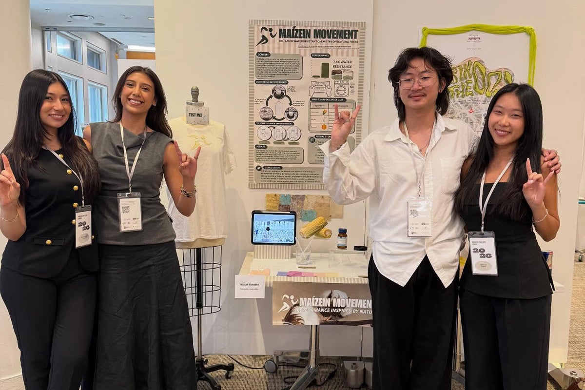 Four college students stand next to a display descirbing their research