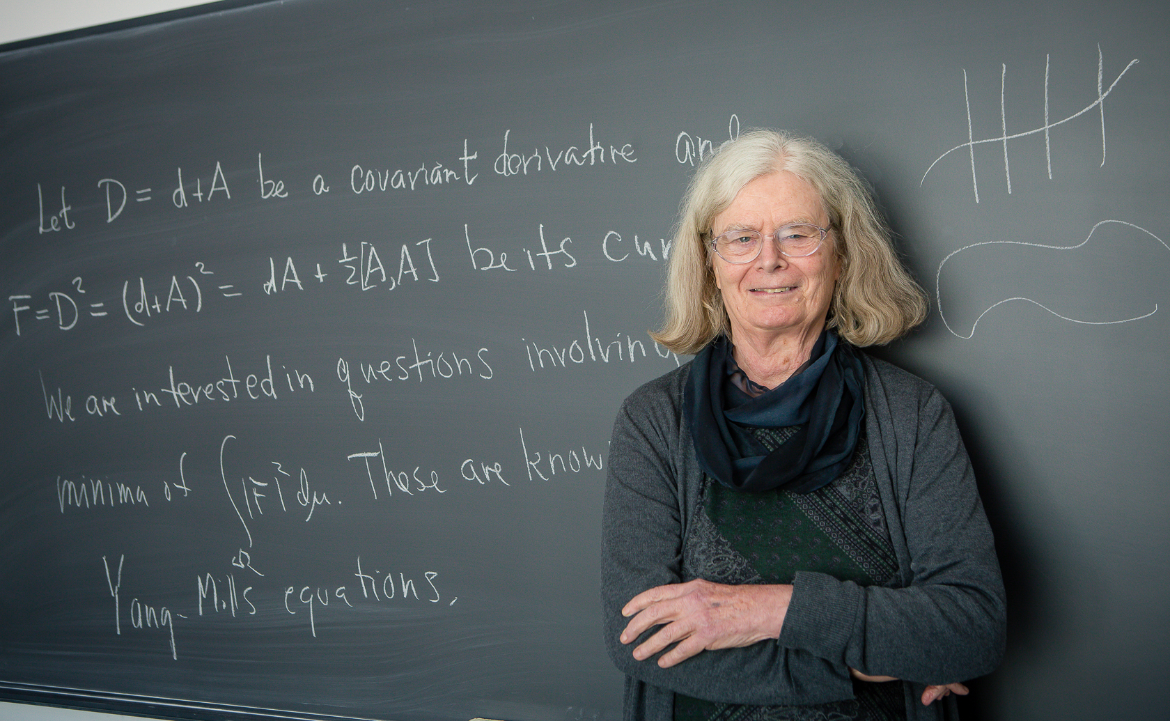 Karen Uhlenbeck stands in front of a blackboard with mathematical formulas written in chalk behind her