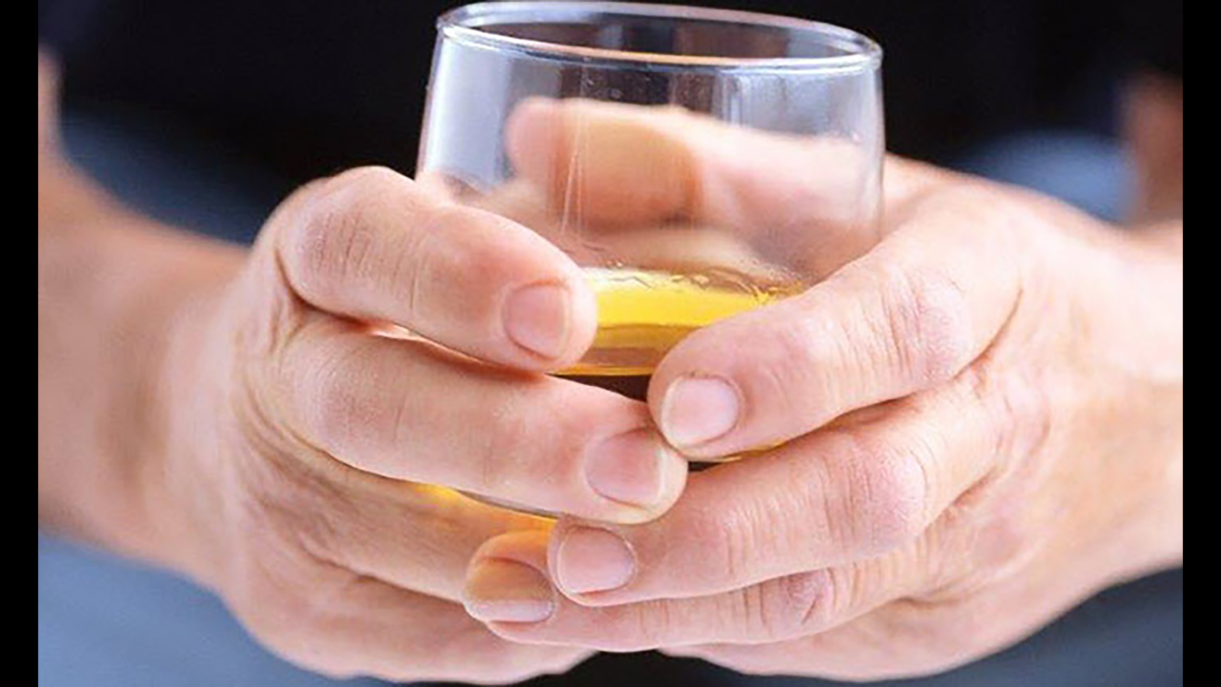 A pair of hands holding a glass of semi-clear yellowish liquid