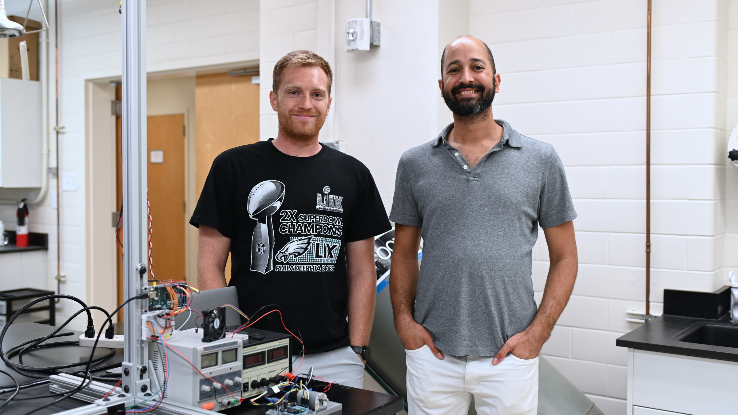 John McGrath (left) and Jose Alvarado (right) stand in front of a lab bench on which machinery sits