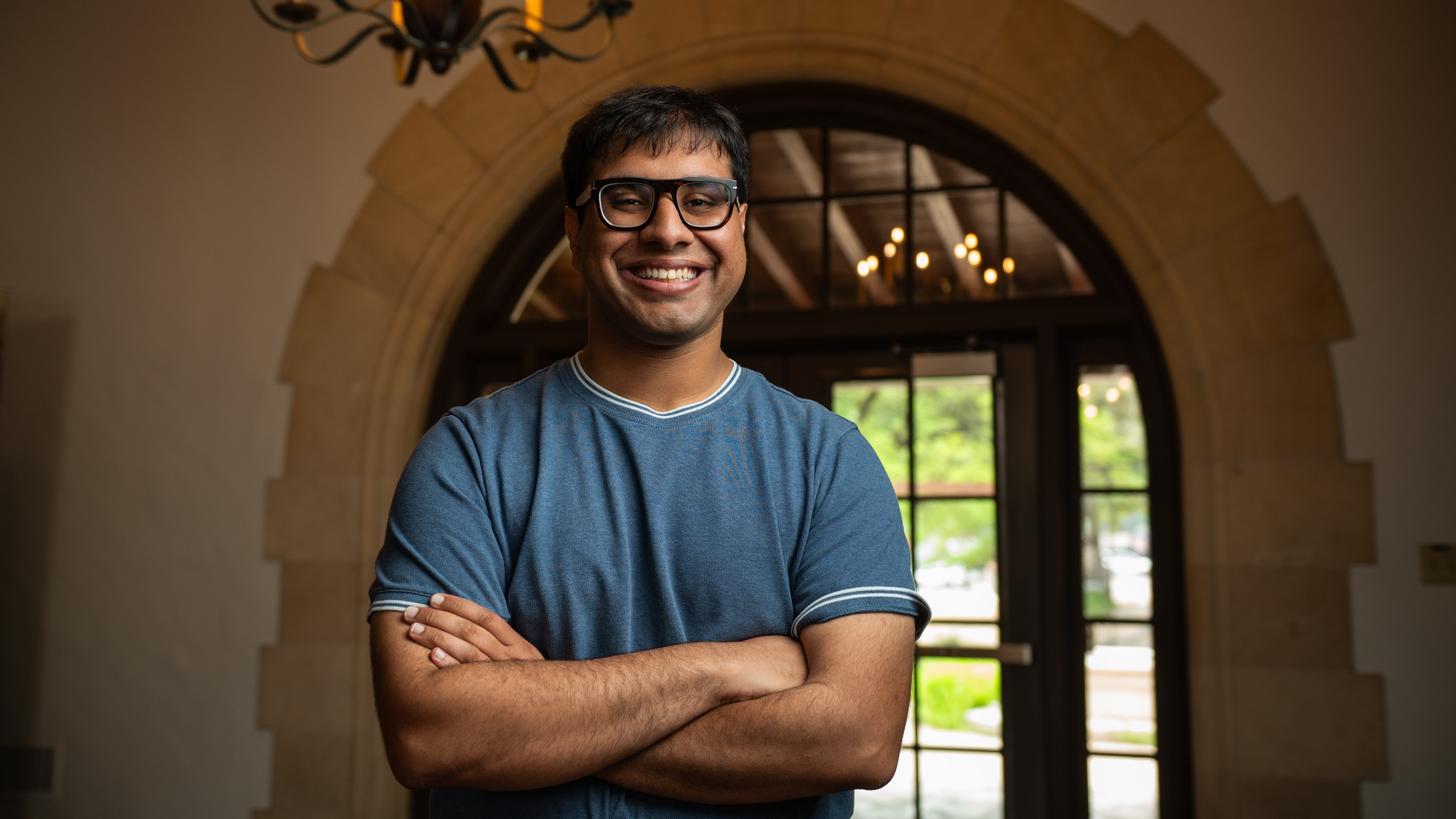 A college student with short dark hair and folded arms, wearing a blue shirt and glasses