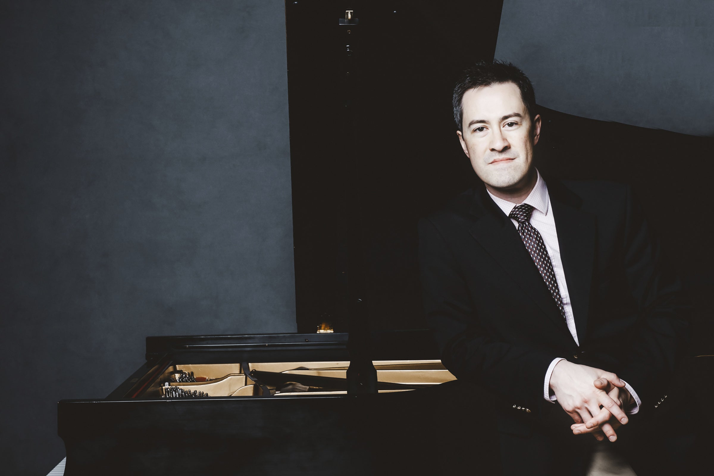 Andrew Brownell leans against a piano