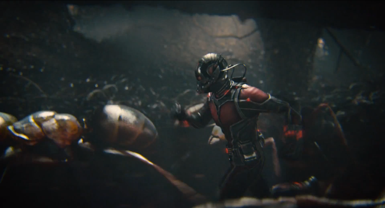 A man in a red and black superhero costume runs through a swarm of ants larger than himself