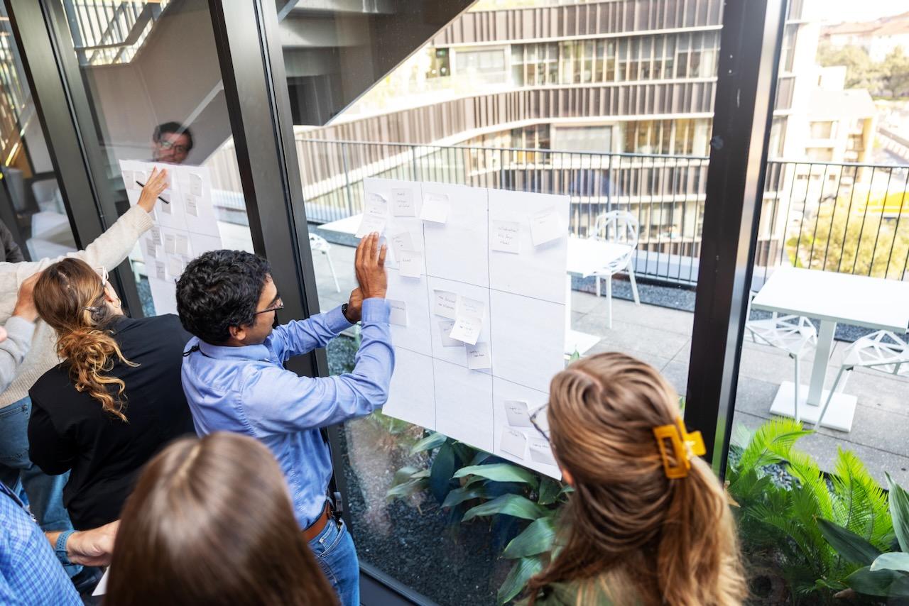 Faculty members stick small notes onto poster boards on windows during a design thinking workshop