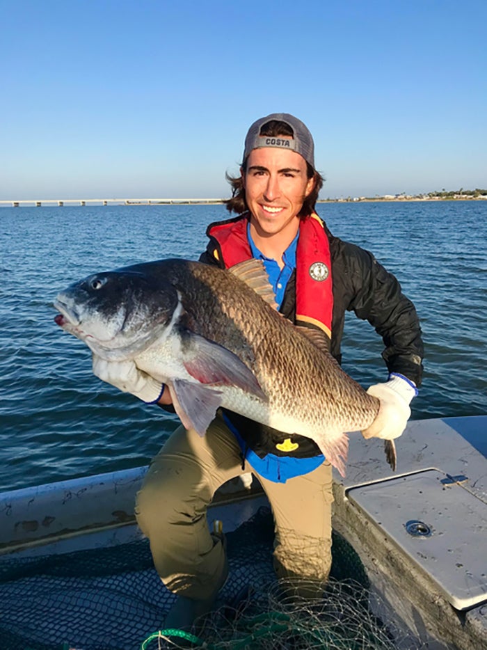 A man stands on a boat holding a very large fish