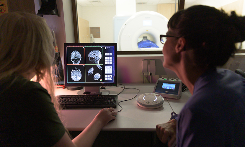 Two scientists look at a computer monitor with brain scan images