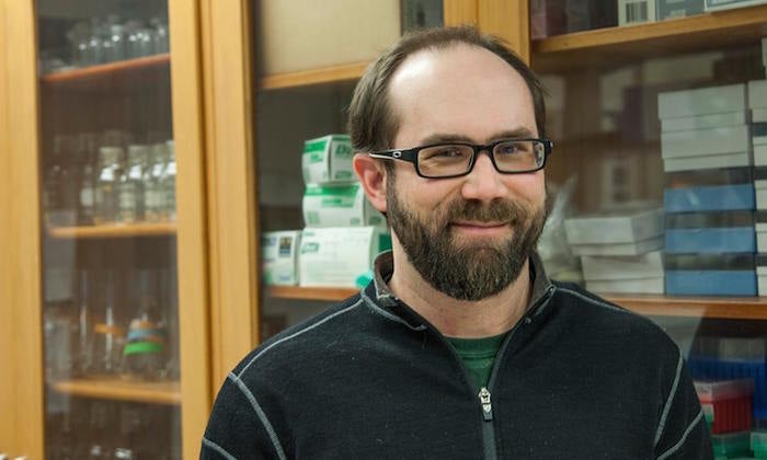 Brett Baker in a zippered shirt stands in a lab in front of cabinets