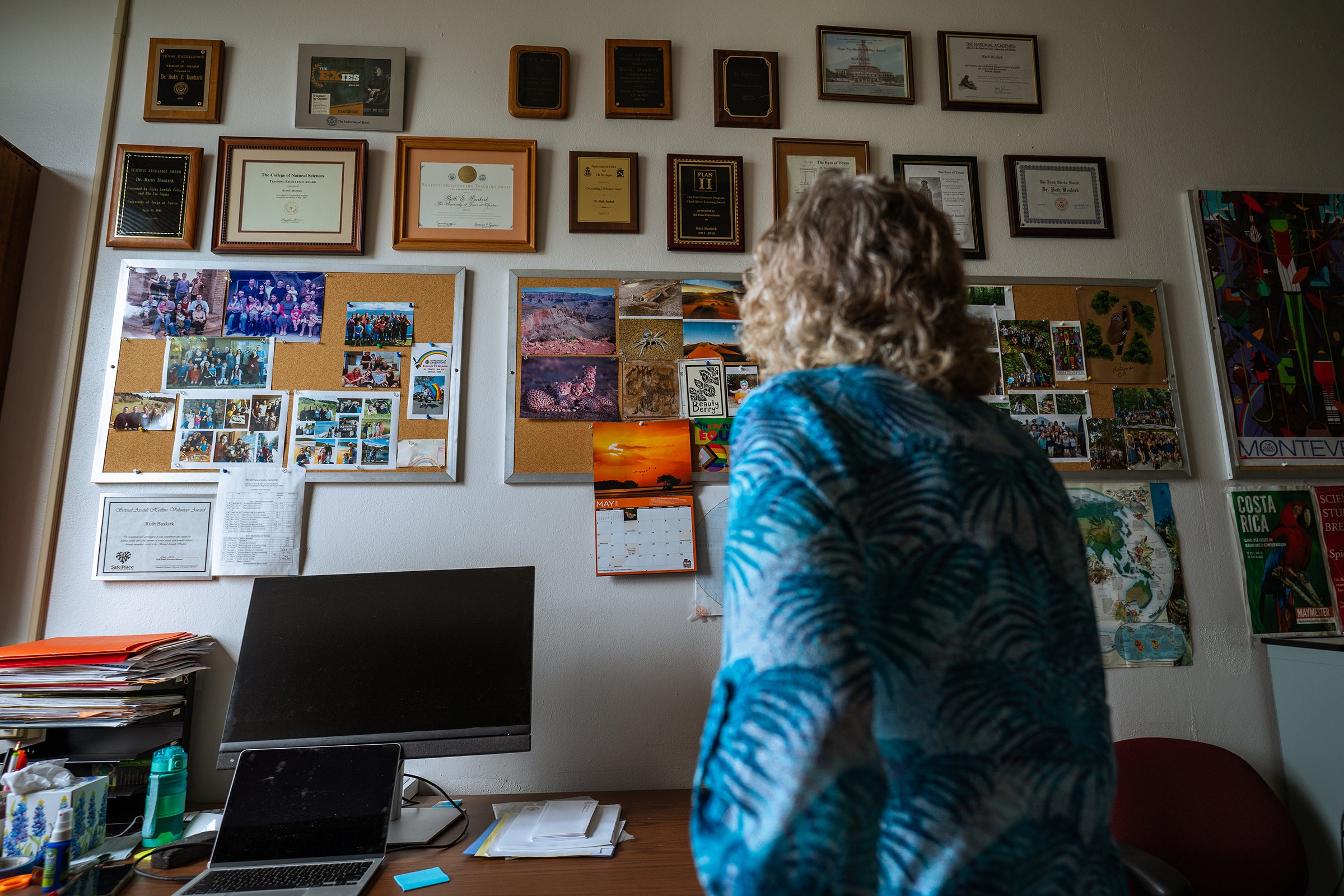 A professor looks at a wall of framed certificates and photos