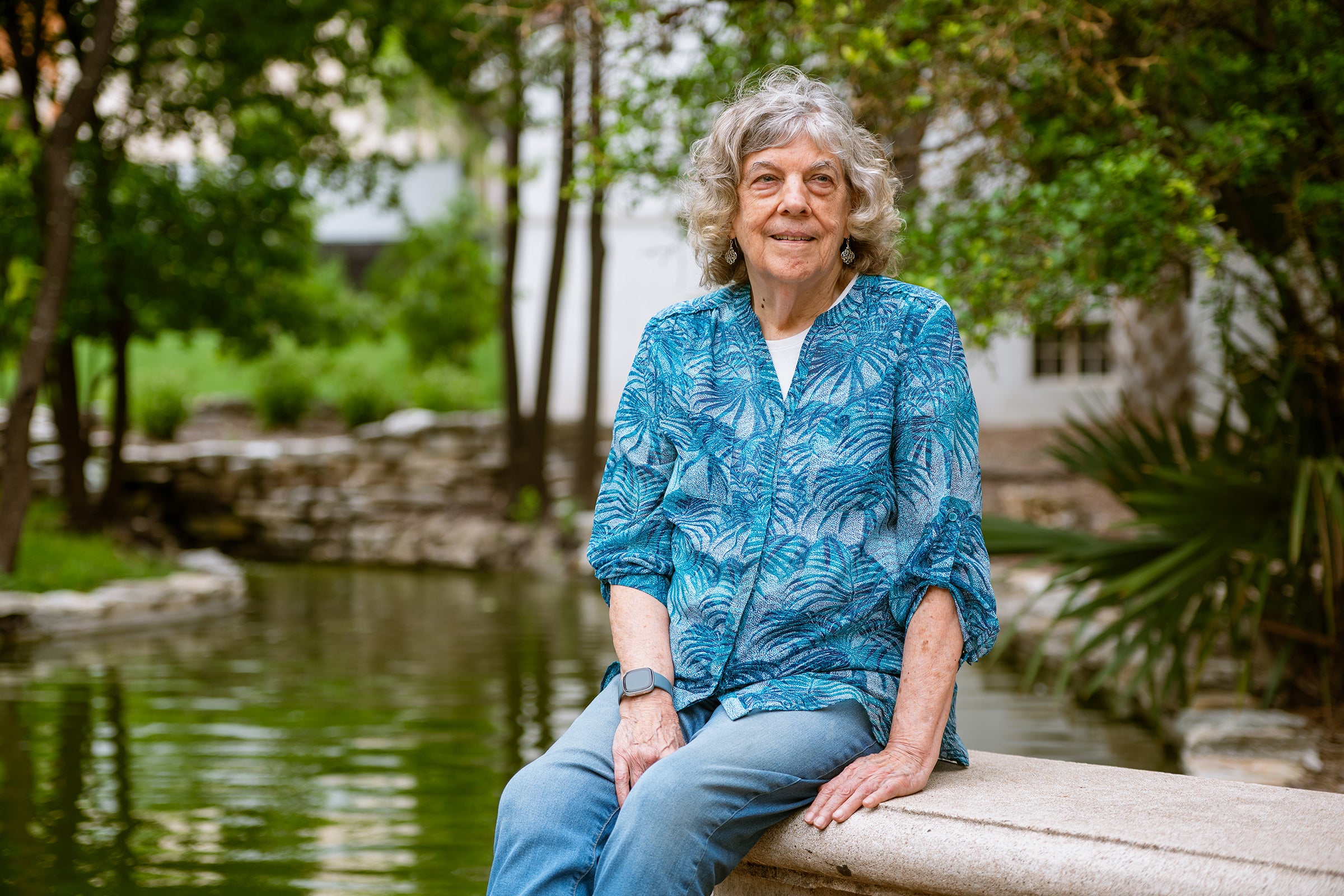 A scientist sits on a bench in front of a pond and trees