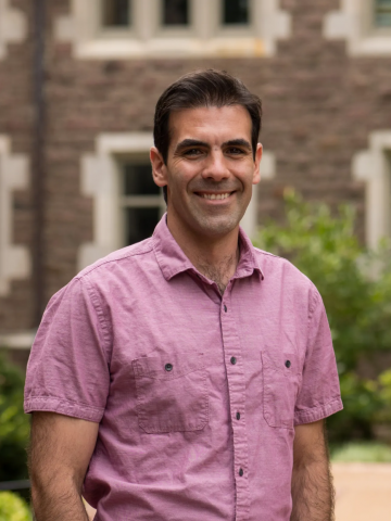 Carlos Botero wearing a fuschia shirt and smiling in front of a brick building