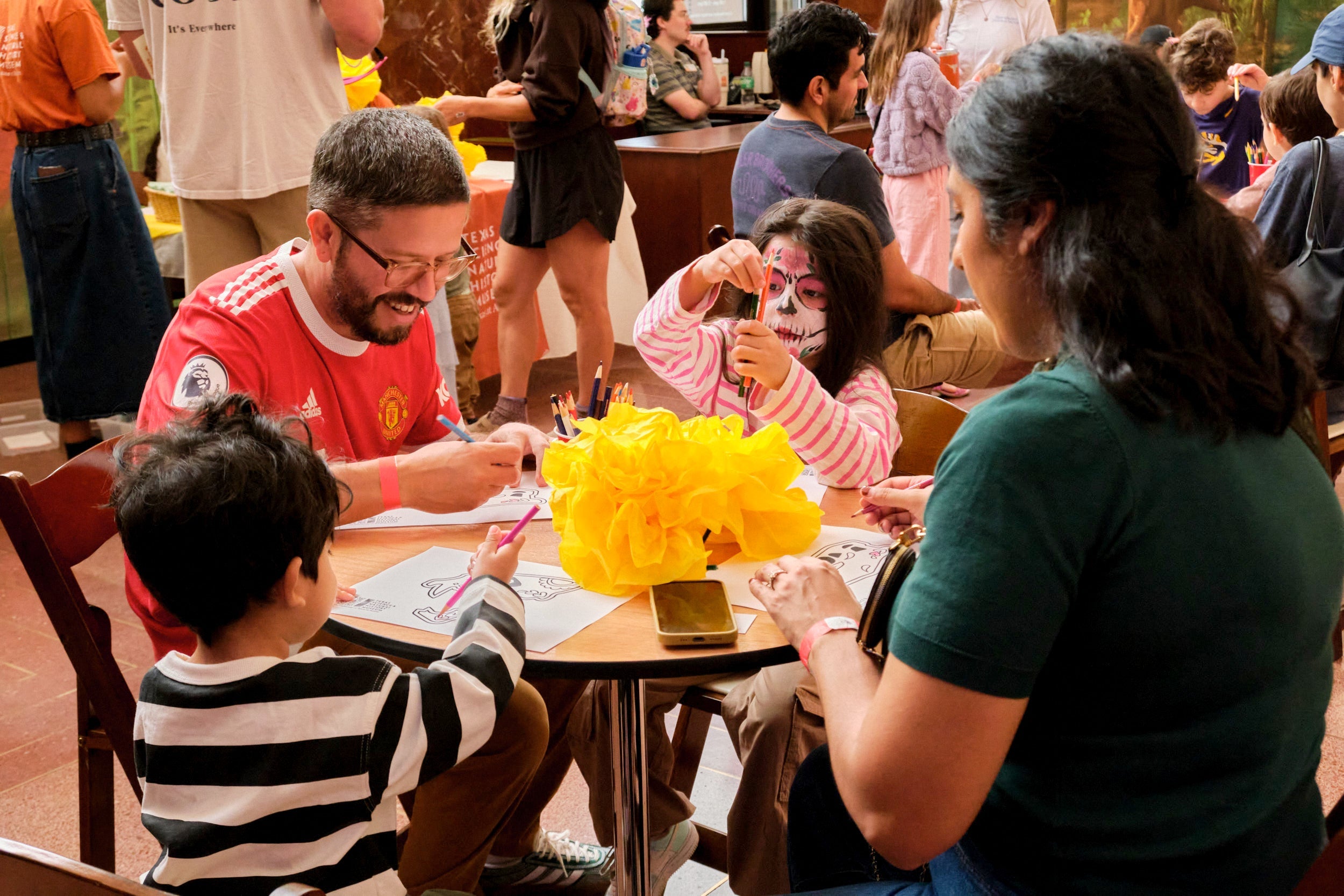A family sits around a table doing Día de los Muertos crafts together