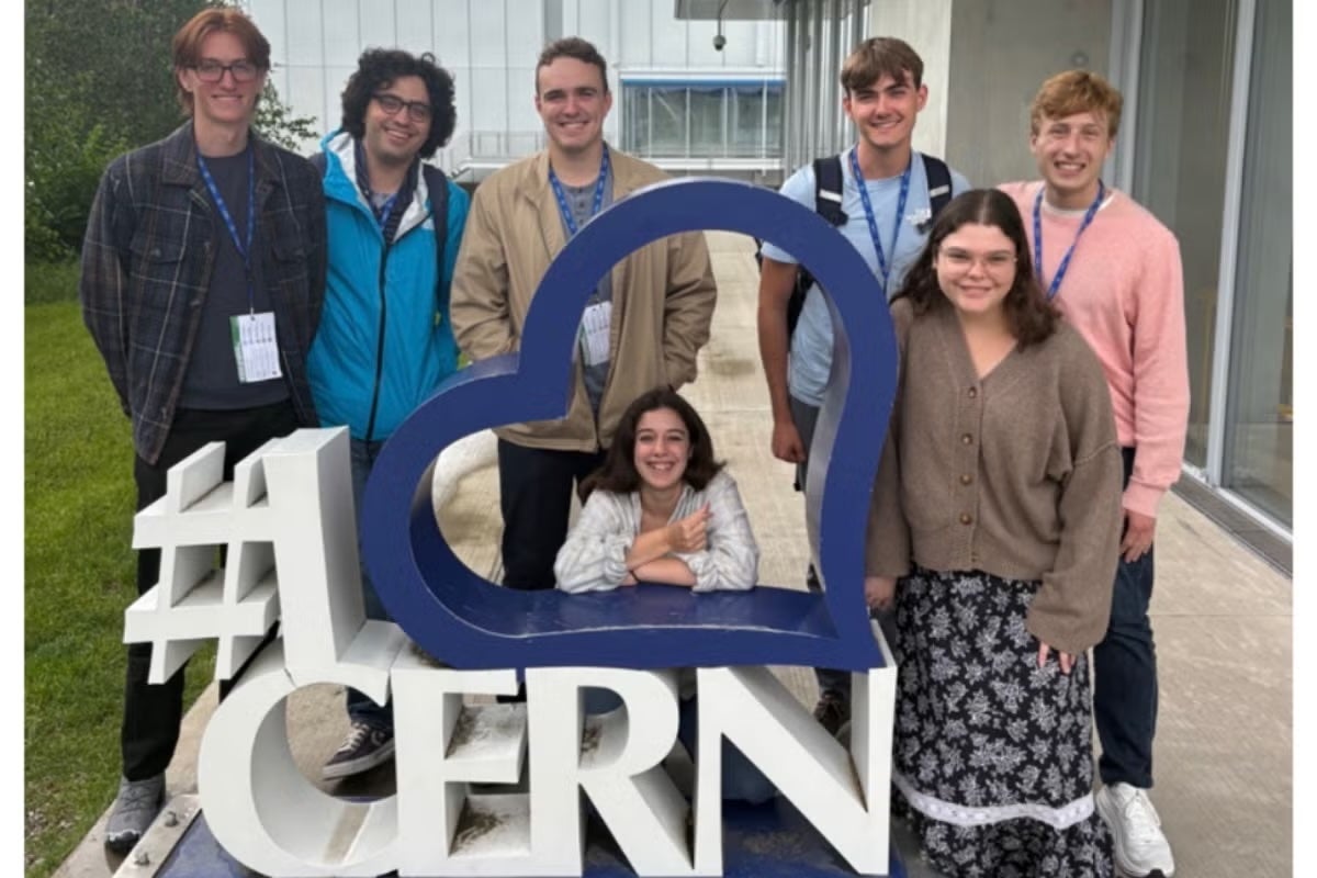 A team of students and researchers pose by a sign that reads #I [Heart] CERN
