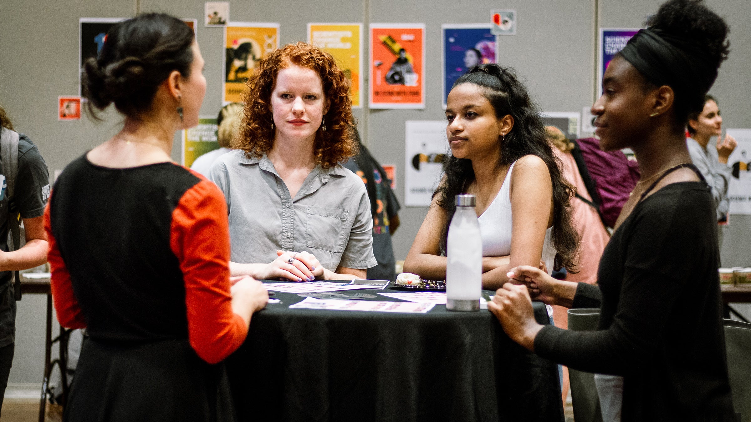 Four women in conversation, standing around a table