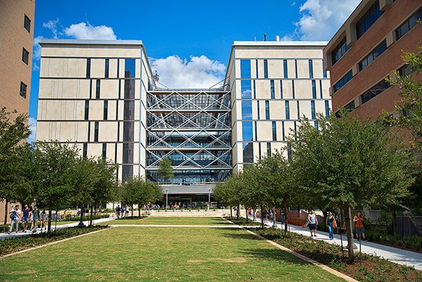 The EERC Building on the UT campus is shown under a blue sky with a tree-lined lawn stretched in front of it and students walking paths in its direction