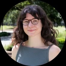 A young woman in glasses smiles in front of a verdant outdoor area