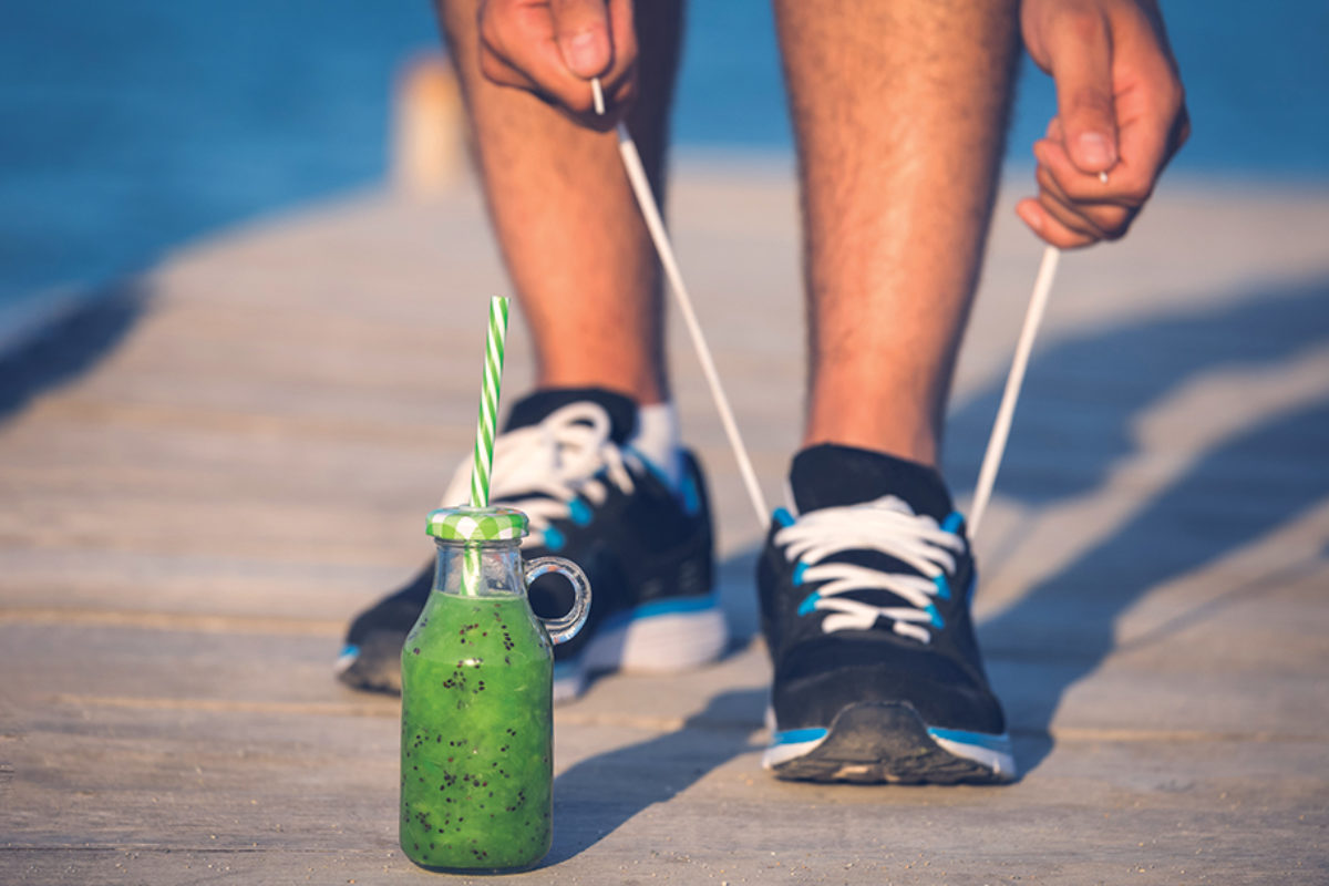 Image of a person wearing running shoes and tying laces with a glass bottle of green smootie