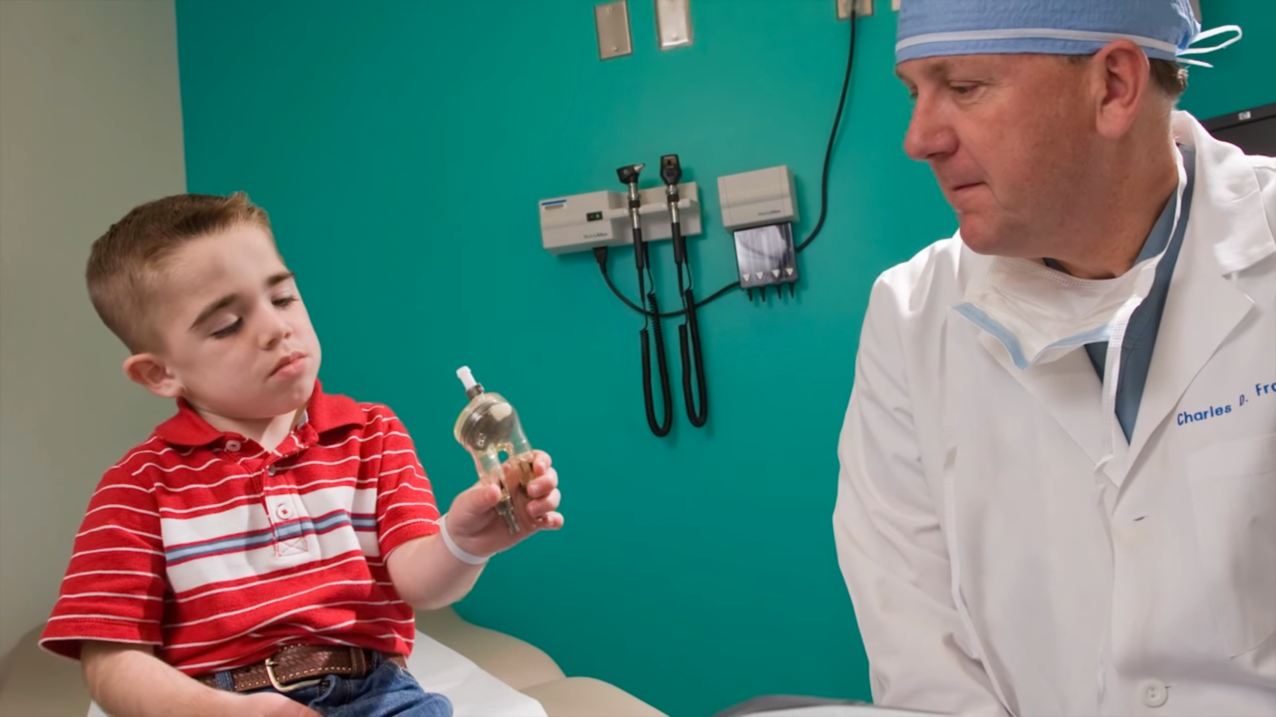 A young boy looks at a mechanical heart pump, as a doctor in white coat watches