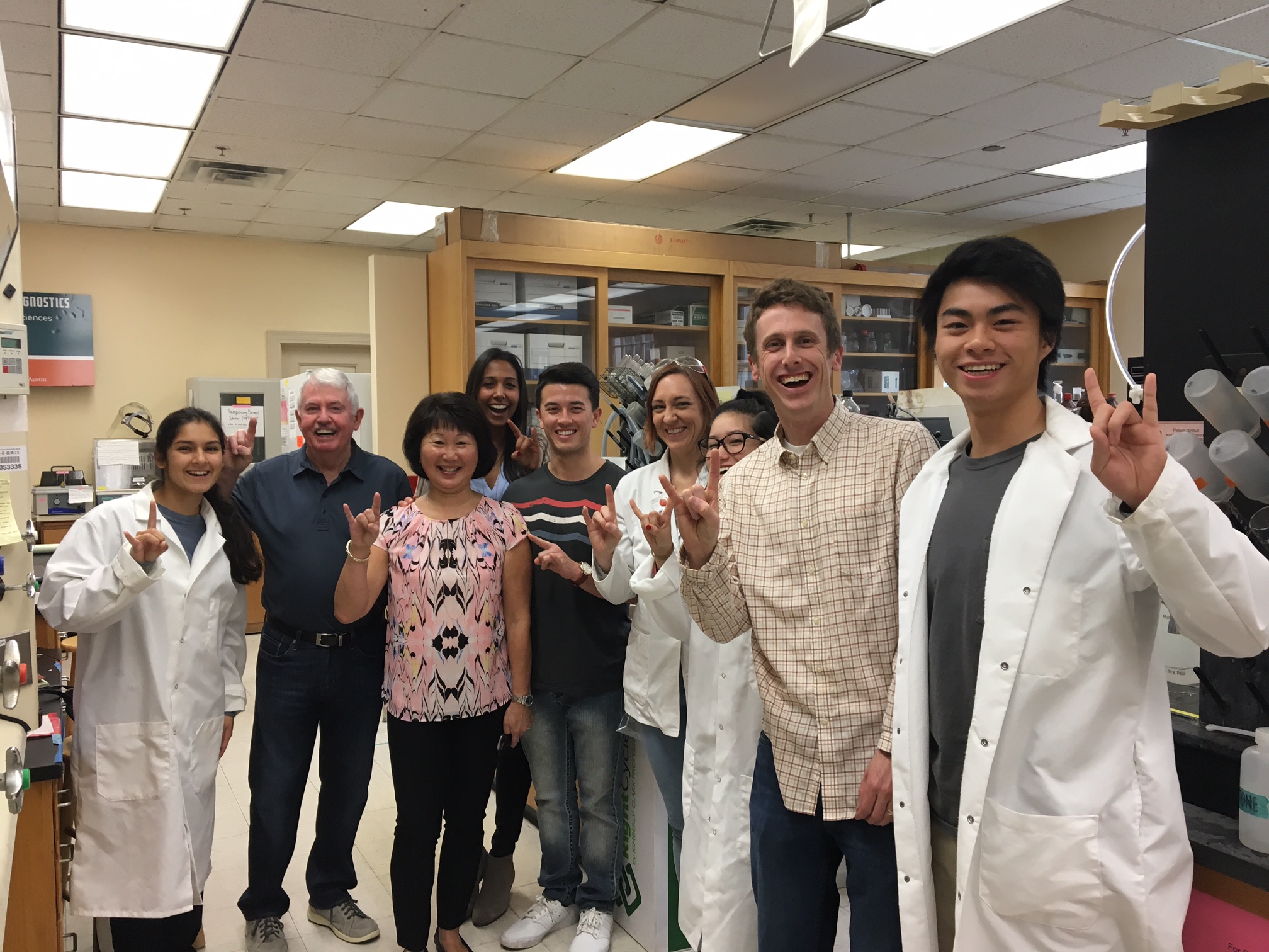 A group of adults and students posing for a photo in a lab, with some students wearing white lab coats
