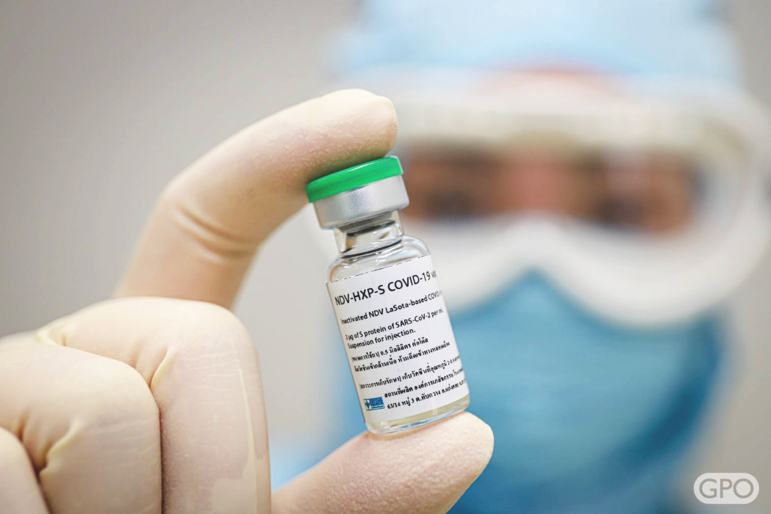 A masked person holds a glass vial of vaccine