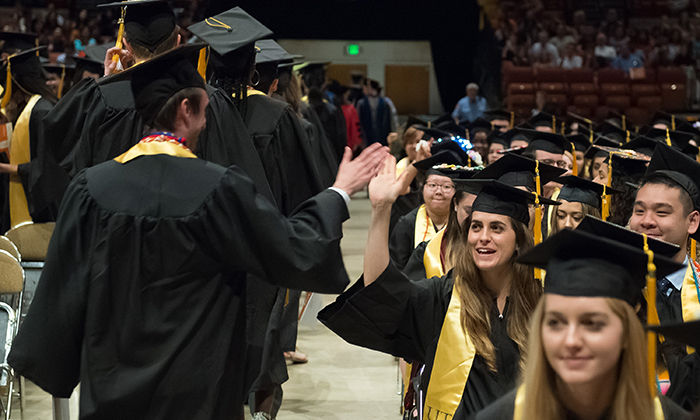 Students in graduation robes high five each other