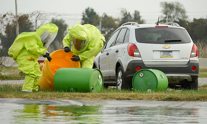 People in yellow hazmat suits pick up barrels of chemical waste