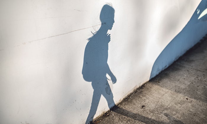 Shadow of a young person wearing a backpack on a white wall