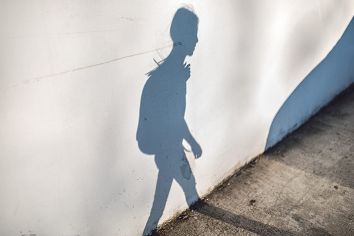 Shadow on a white wall of a young person walking with a backpack