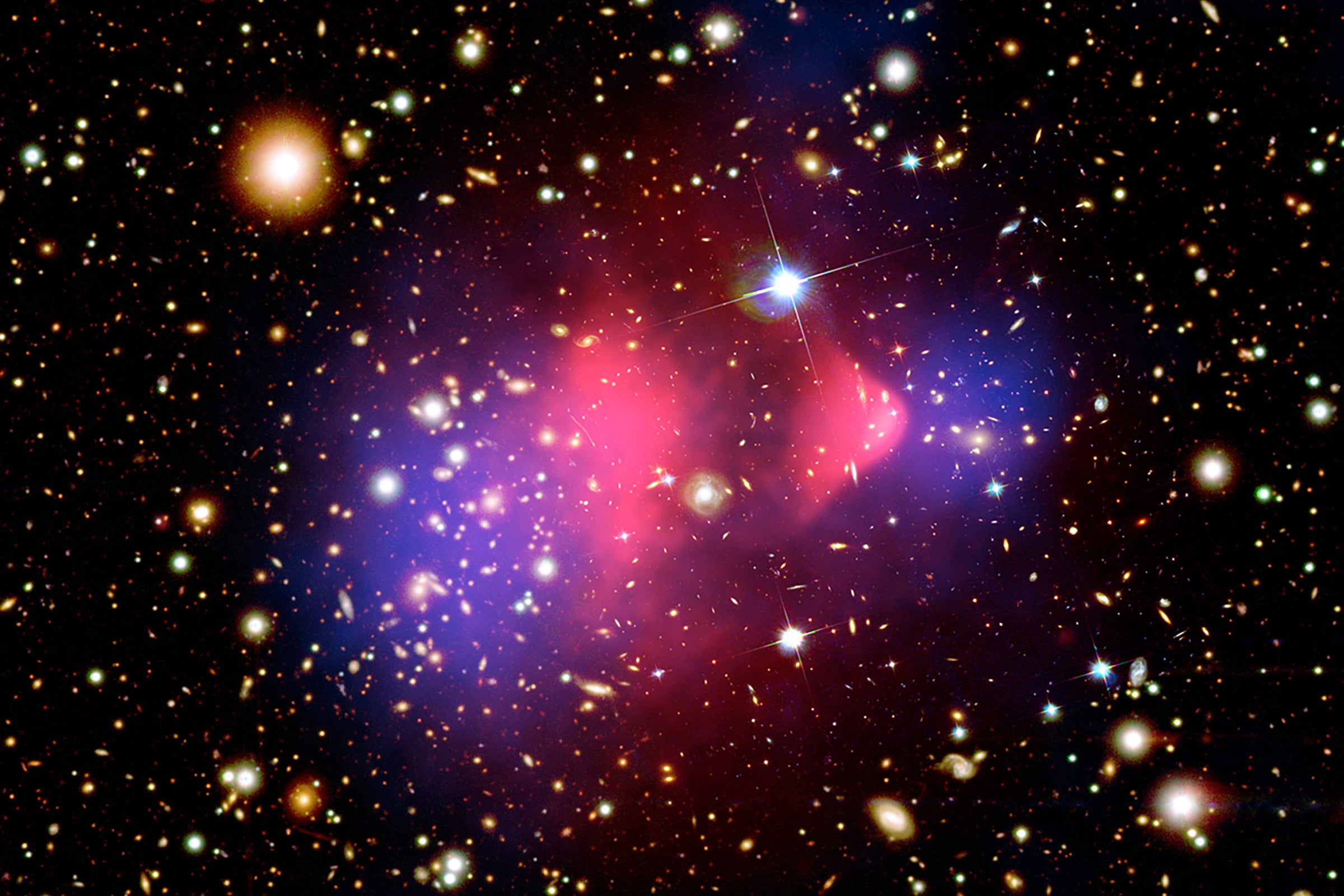 Composite image of matter in galaxy cluster 1E 0657-556, formed by collision of two large galaxy clusters. Hot gas detected by Chandra observatory in X-rays (2 pink clumps) contains most of the baryonic matter. Visible-light image from Magellan telescopes in Chile and Hubble Space Telescope shows the galaxies in orange and white. Blue areas depict where astronomers calculate most of the mass in the clusters must be—direct evidence that nearly all of the matter in the clusters is dark. Image from NASA.