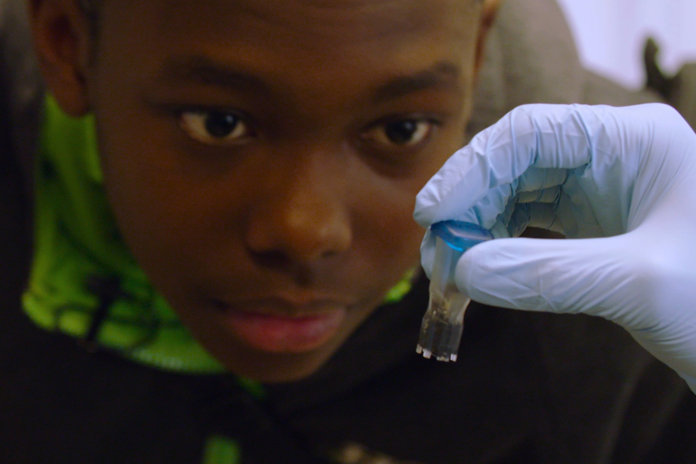 A young child looks at a small test tube held by a gloved hand.