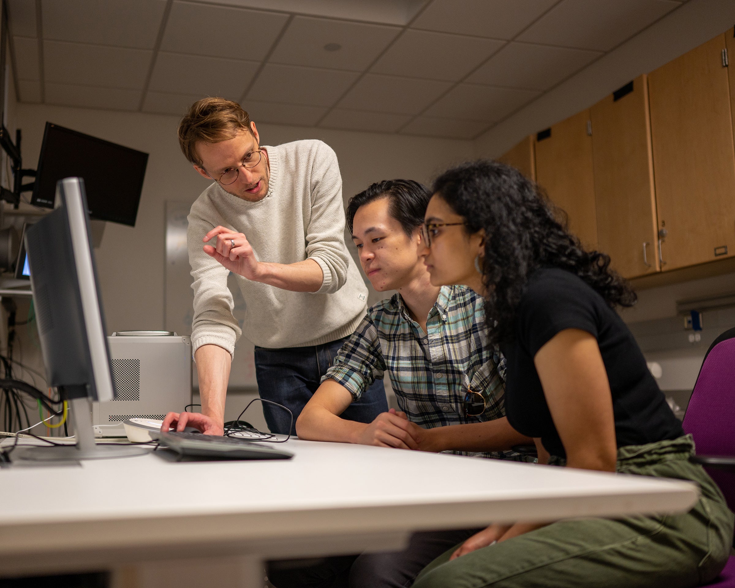 Three scientists discussing their work at a computer station