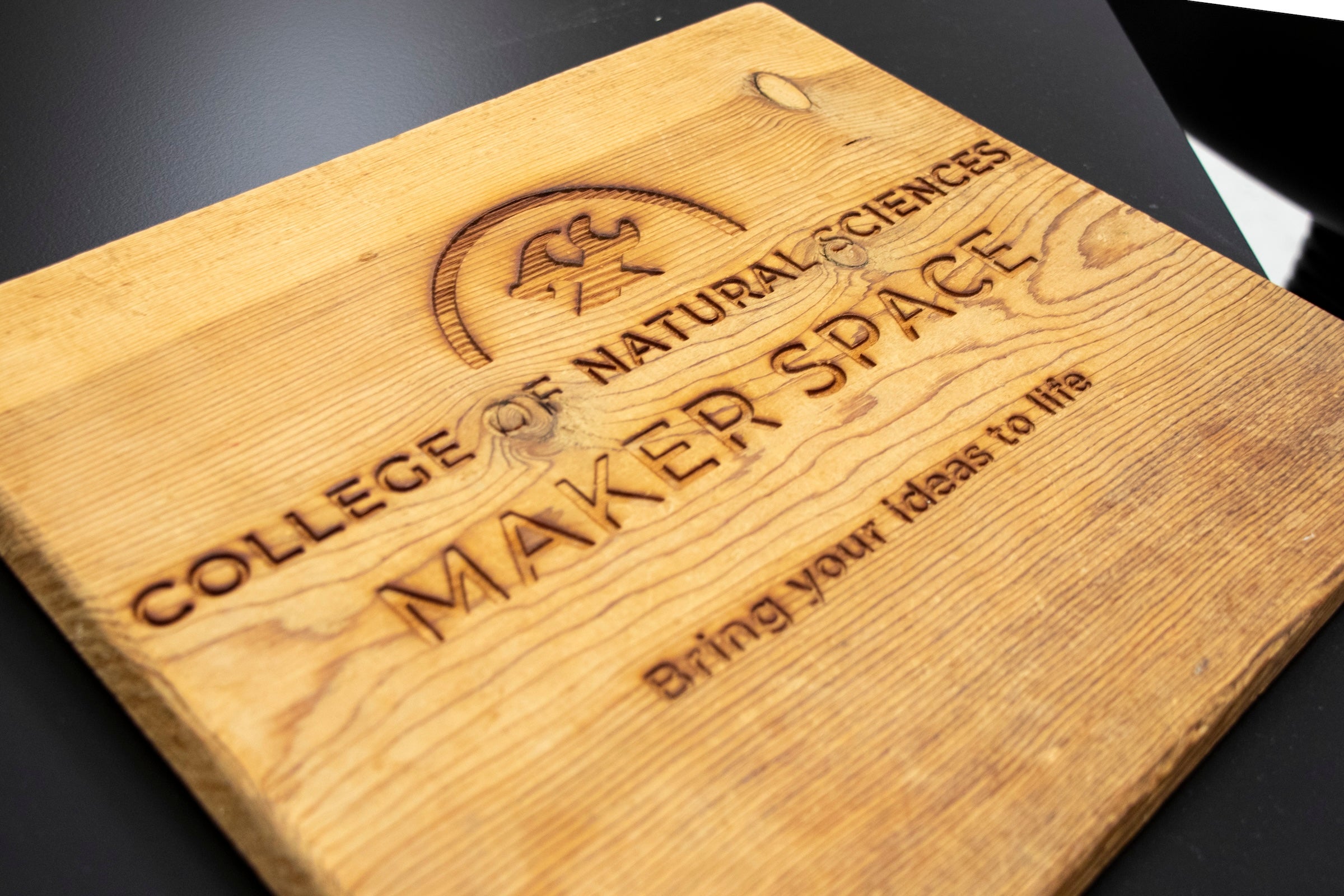 A wooden slab has an imprint of a wrench and a hammer over words "College of Natural Sciences Maker Space: Bring your ideas to life"