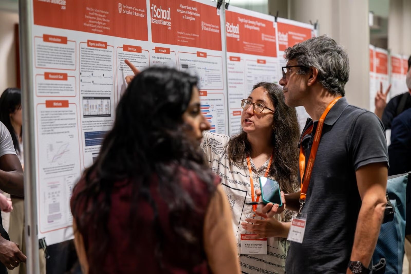 Three people cluster around an iSchool research poster to discuss results.